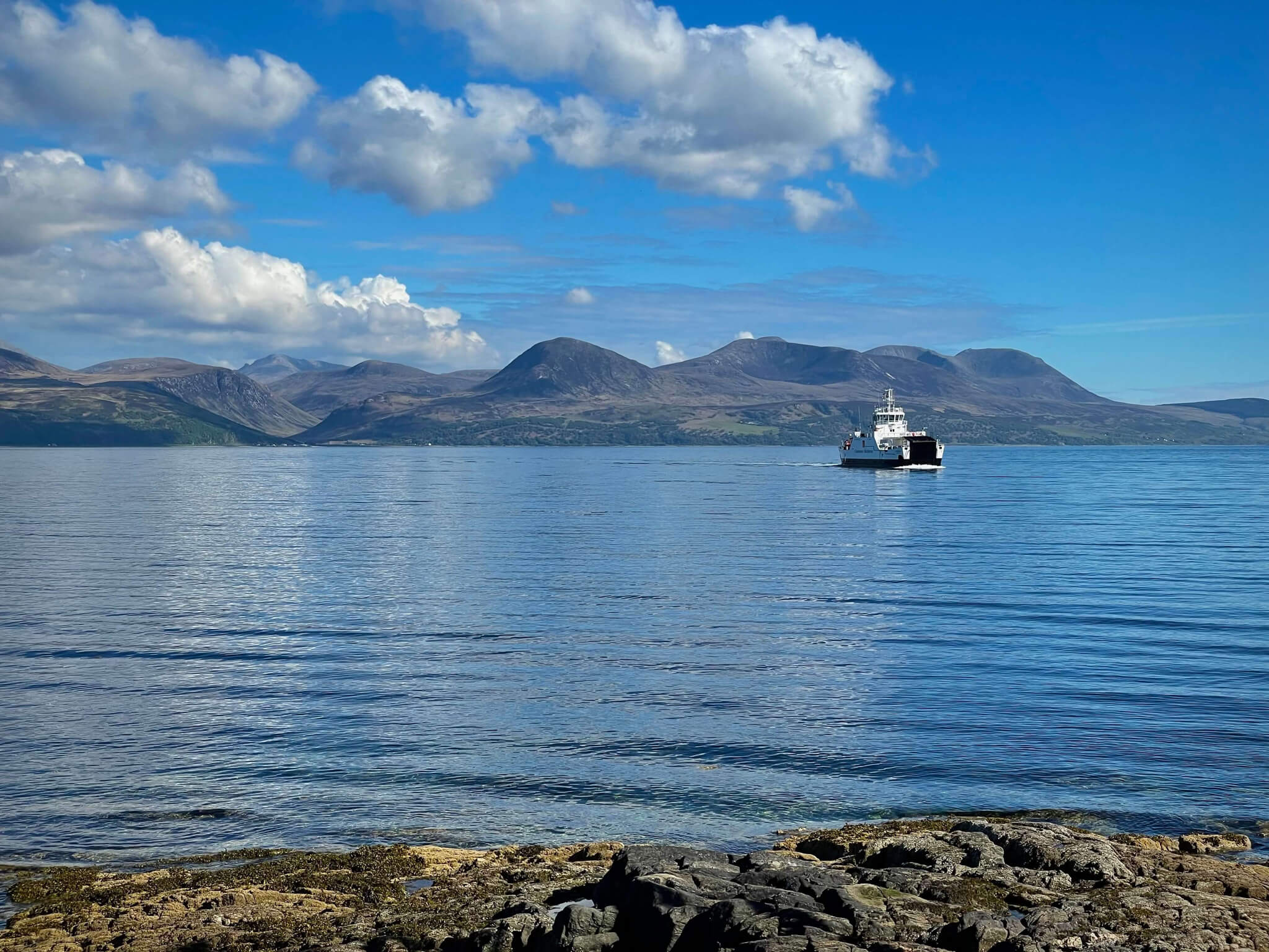 a ferry on the sea approaching Arran Mountain range in Scotland