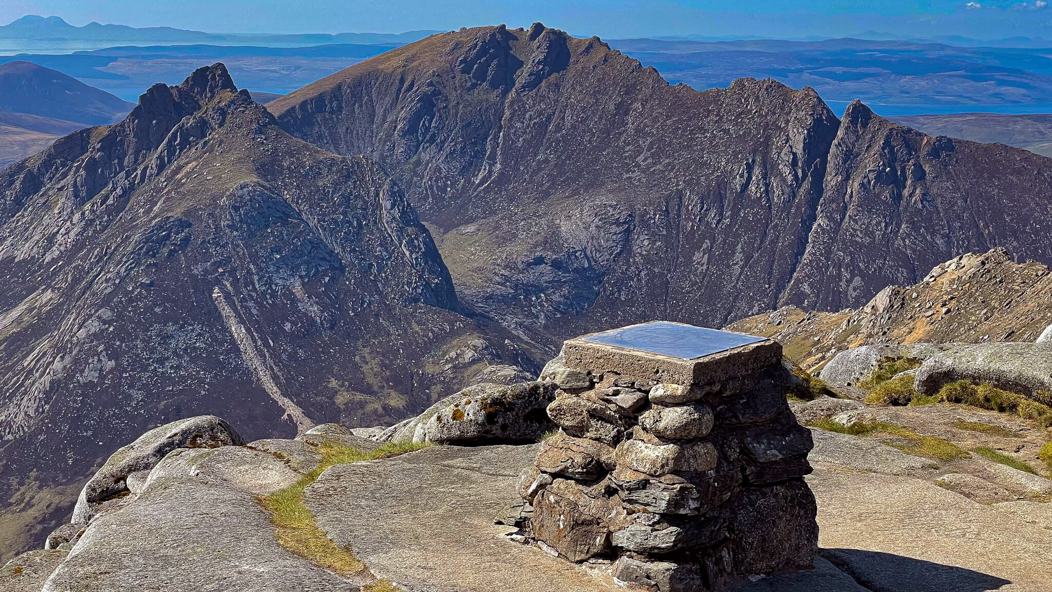 View from the Goatfell summit of Isle of Arran in Scotland. Stone trig point with Arran Mountain range in the background.